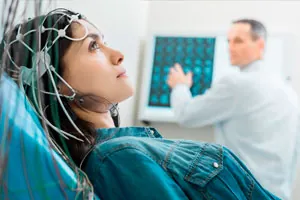 Mulher com touca de eletrodos na cabeça enquanto o técnico acompanha o exame no monitor.