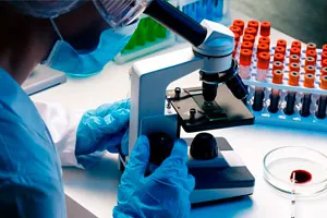 Microscópio de laboratório ao lado de uma estante com tubos de coleta.