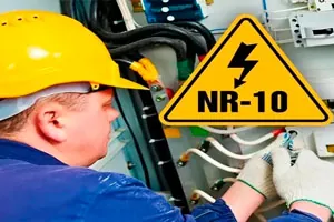 Eletricista de capacete amarelo trabalha num painel, com a placa de alerta NR-10 ao lado.