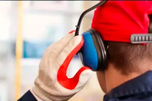Trabalhador de capacete vermelho e luvas coloca o protetor auricular tipo concha.
