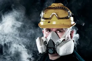 Trabalhador com máscara respiratória e óculos de proteção em meio à fumaça.