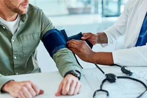 Profissional de saúde mede a pressão arterial de um trabalhador sentado à mesa.